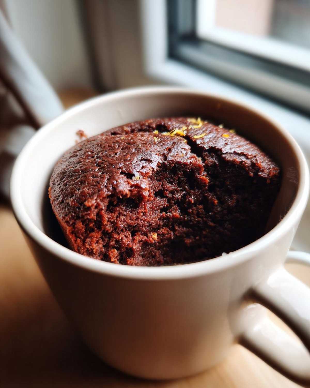 A close-up of a rich Chocolate Orange Mug Cake, slightly cracked on top with orange zest.