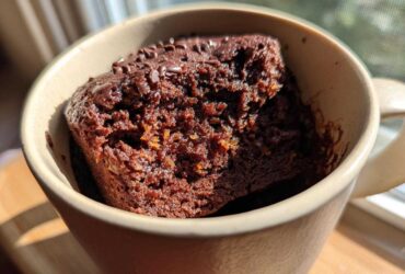 Close-up of a rich Chocolate Orange Mug Cake in a tan mug, topped with chocolate sprinkles.
