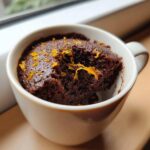 Close-up of a moist Chocolate Orange Mug Cake topped with fresh orange zest, with a bite taken out.