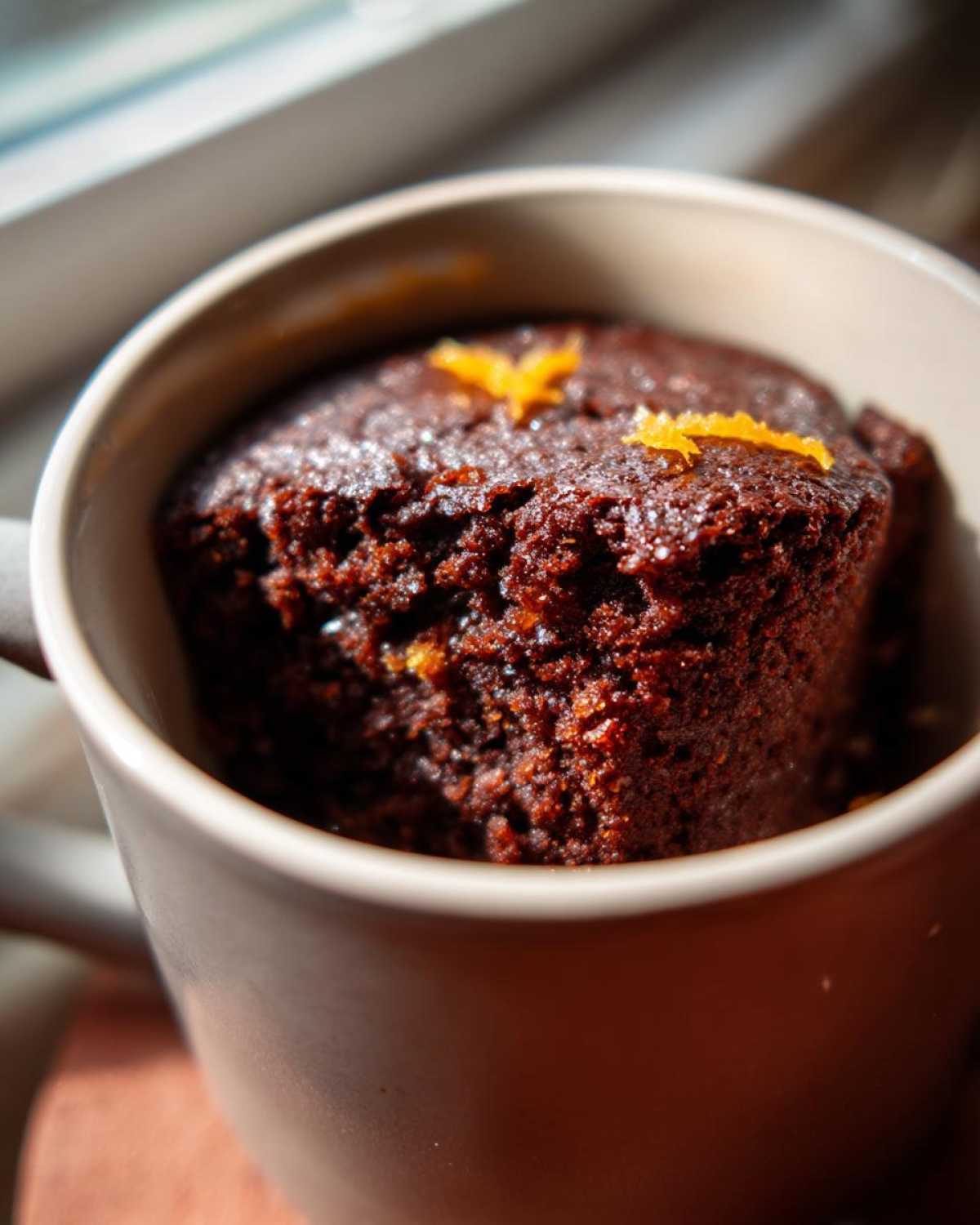A close-up of a moist Chocolate Orange Mug Cake topped with fresh orange zest.