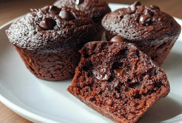 Close-up of moist chocolate protein muffins topped with chocolate chips, one muffin is broken in half revealing melted chocolate.