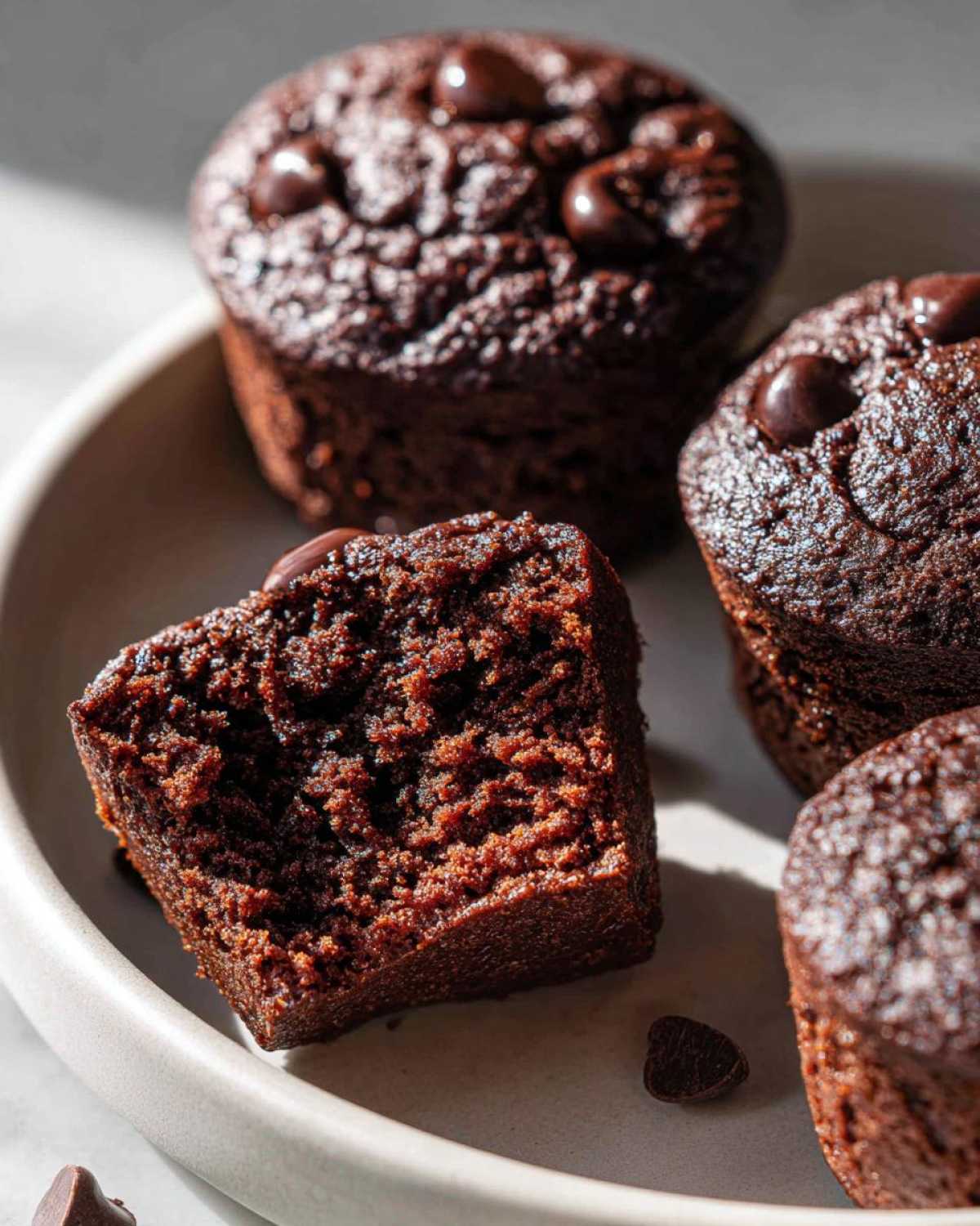 A close-up view of a chocolate protein muffin, cut in half, revealing a moist interior and chocolate chips.