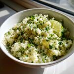 A white bowl filled with fluffy Cilantro Lime Cauliflower Rice, garnished with fresh cilantro and a lime wedge.