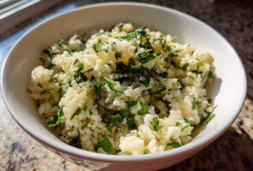 A white bowl filled with freshly prepared Cilantro Lime Cauliflower Rice, garnished with chopped cilantro.