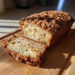 A delicious slice of cinnamon streusel topped zucchini bread on a wooden board, with the rest of the loaf behind it.