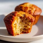 A close-up of a classic banana muffin with a bite taken out, showing its moist texture.