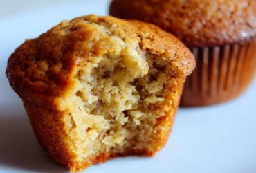 Close-up of a Classic banana muffin with a bite taken out, revealing a moist interior. Another muffin is in the background.