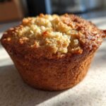 A single, golden-brown Classic Protein Muffin with a crumbly topping, sitting on a speckled countertop.