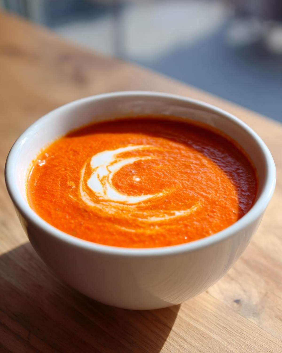A bowl of vibrant Creamy Roasted Red Pepper Soup with a swirl of cream on top.