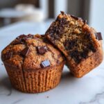 Close-up of two double chocolate chip muffins, one halved to reveal a moist interior packed with chocolate chips.