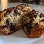 A close-up view of a double chocolate chip muffin, split in half to reveal a moist interior packed with chocolate chips.