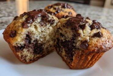 A close-up view of a double chocolate chip muffin, split in half to reveal a moist interior packed with chocolate chips.