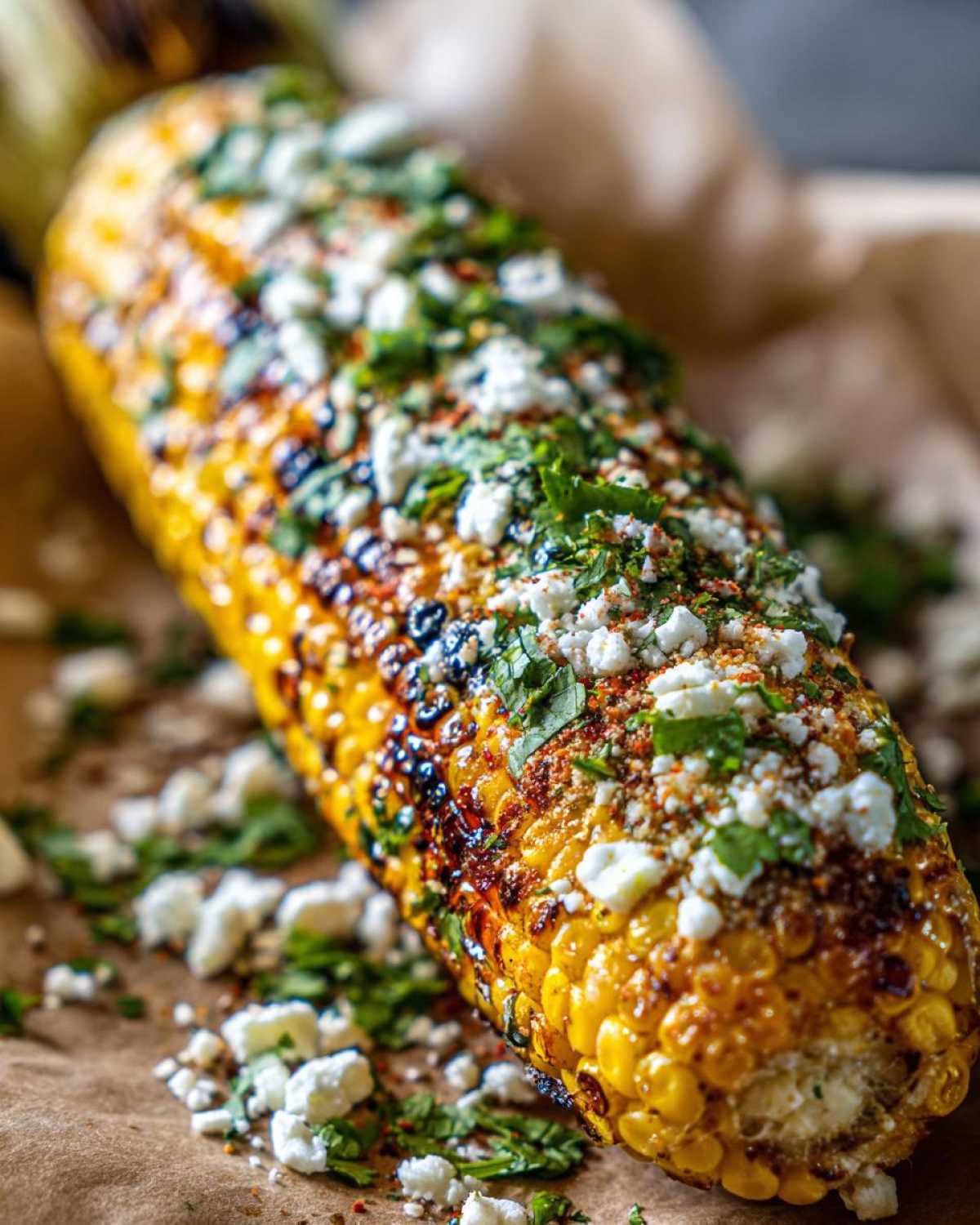 Close-up of a grilled corn cob, prepared with a perfect Elote recipe, topped with crumbled cotija cheese, fresh cilantro, and chili powder.