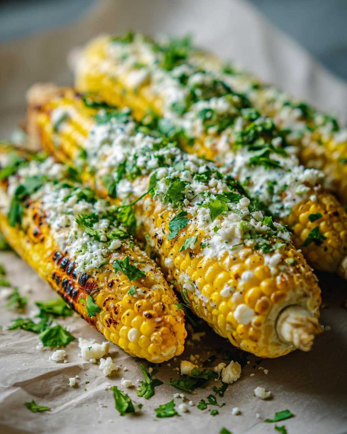 Close-up of grilled corn on the cob, generously topped with crumbled cheese, cilantro, and spices, showcasing a perfect Elote recipe.
