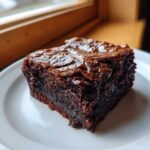A close-up of a rich, fudgy espresso brownie slice on a white plate, showcasing its moist texture.