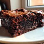 A close-up of a rich, fudgy espresso brownie slice on a white plate, showcasing its moist texture.