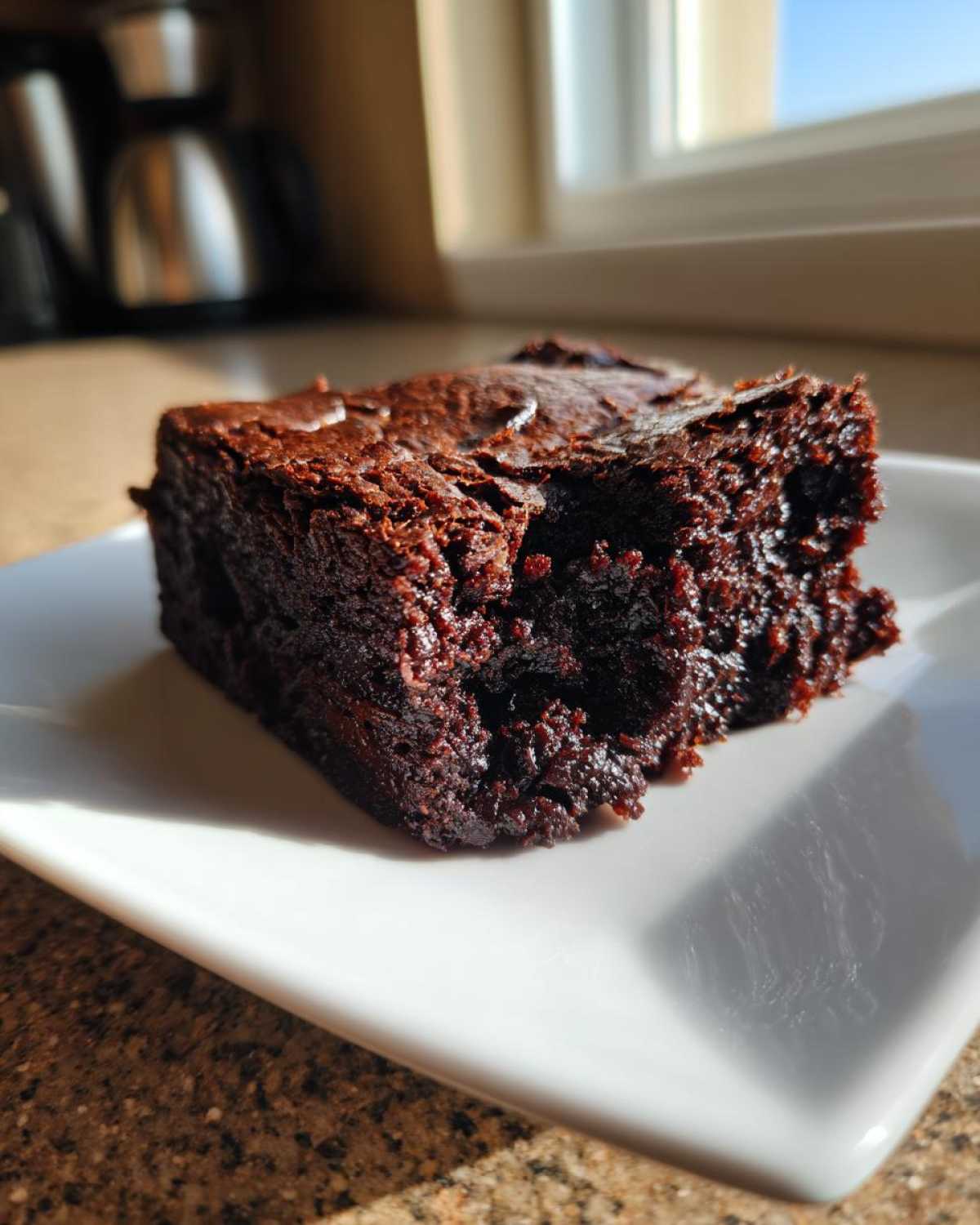 A close-up of a rich, fudgy espresso brownie on a white plate, showcasing its moist texture.