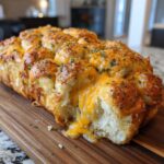 A golden brown Everything Bagel Pull Apart Loaf with melted cheese oozing out, topped with herbs and spices.