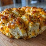 A golden brown Everything Bagel Pull Apart Loaf covered in melted cheese and seasonings on a wooden board.