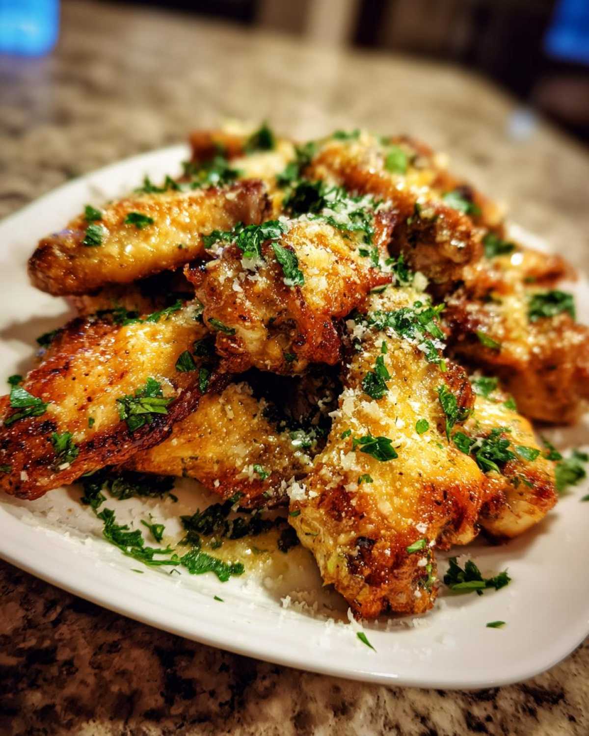 A close-up shot of golden brown Garlic Parmesan Wings sprinkled with fresh parsley and grated Parmesan cheese on a white plate.