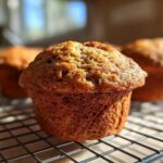 Close-up of a freshly baked gluten-free banana muffin with a golden-brown, textured top, resting on a wire cooling rack.
