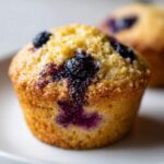 Close-up of a golden-brown gluten-free blueberry muffin bursting with juicy blueberries.