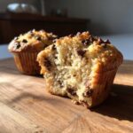 A close-up of a delicious gluten-free chocolate chip muffin, broken in half to show the moist interior and chocolate chips.