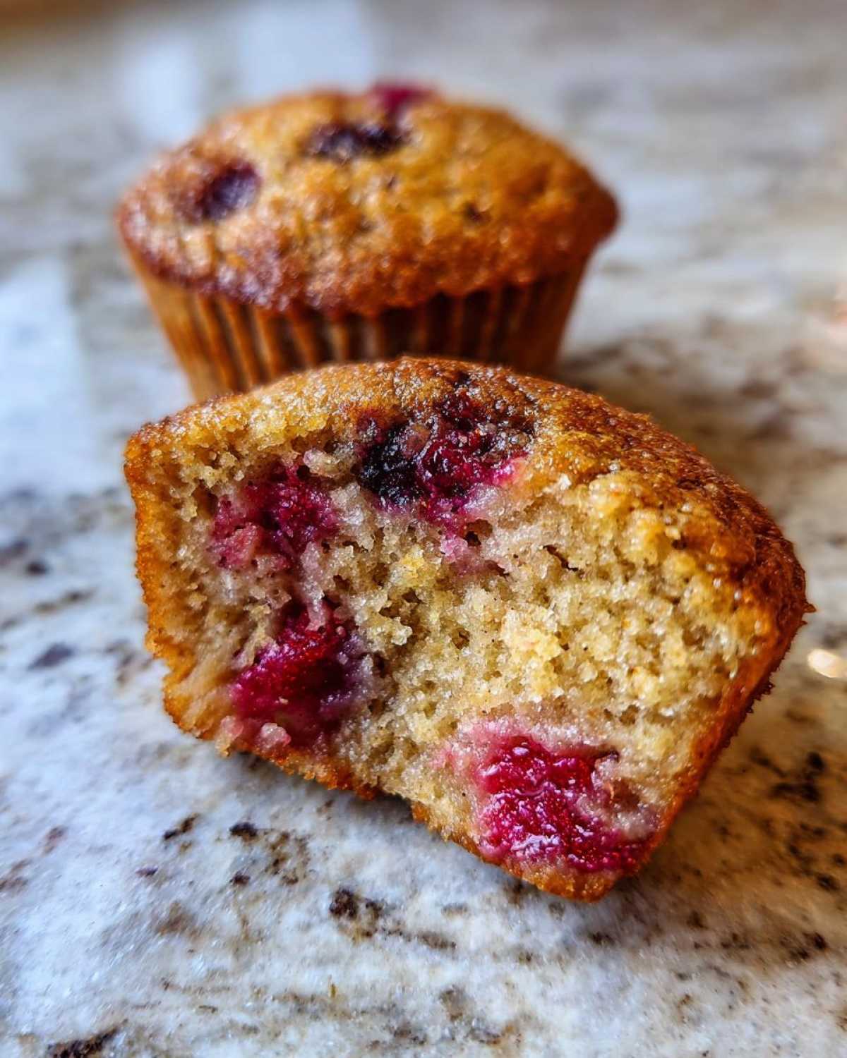Close-up of a gluten-free protein muffin, split in half, revealing juicy berries inside.