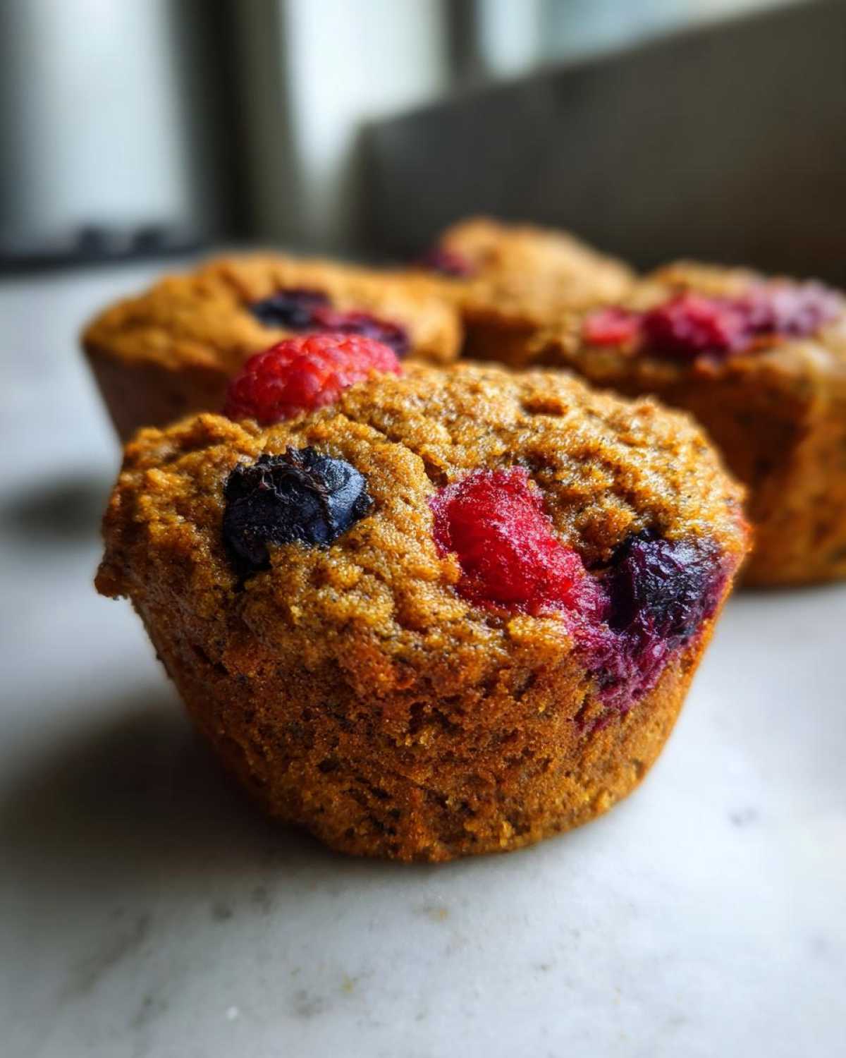 Close-up of delicious gluten-free protein muffins topped with fresh raspberries and blueberries.