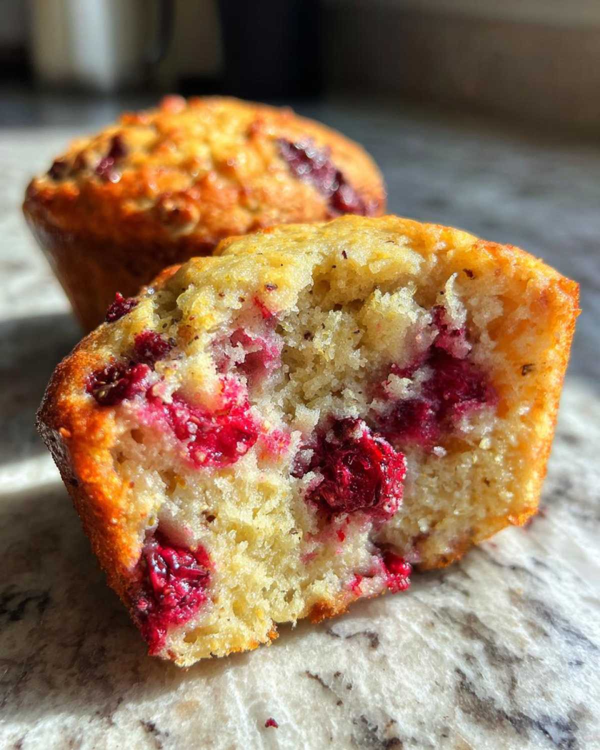 Close-up of a gluten-free protein muffin cut in half, revealing a fluffy interior packed with raspberries.