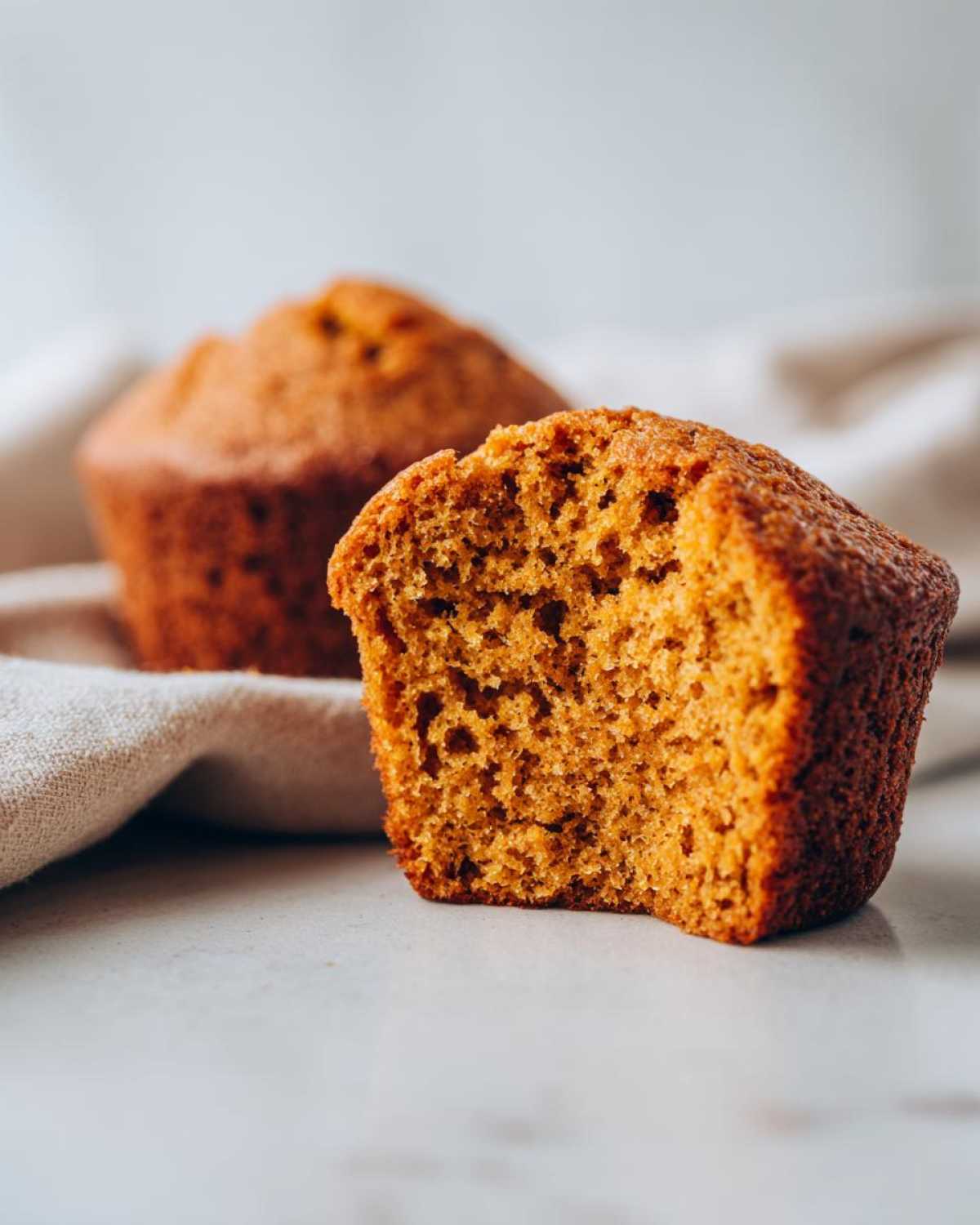 A close-up of a delicious gluten-free pumpkin muffin with a bite taken out, showing its moist texture.
