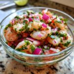 A close-up of a glass bowl filled with vibrant Grapefruit Shrimp Ceviche, featuring plump shrimp, diced tomatoes, red onion, and fresh cilantro.
