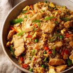 A close-up of a bowl filled with flavorful Hibachi Chicken Fried Rice, featuring tender chicken pieces, scrambled eggs, peas, carrots, and green onions.