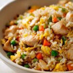 A close-up of a bowl filled with flavorful Hibachi Chicken Fried Rice, featuring tender chicken pieces, fluffy rice, peas, carrots, and scrambled egg.