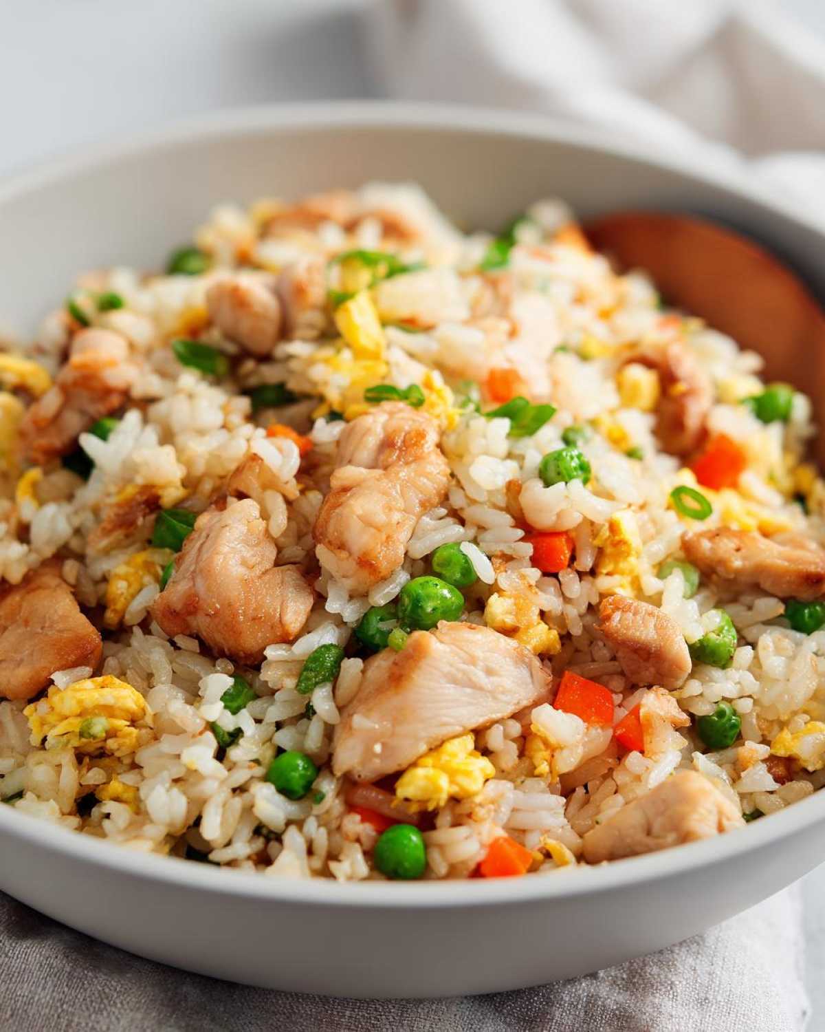 A close-up of a bowl filled with Hibachi Chicken Fried Rice, featuring tender chicken pieces, fluffy rice, scrambled eggs, peas, and carrots.