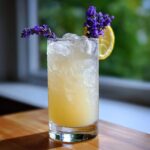 A tall glass filled with ice and Honey Lavender Lemonade, garnished with a lemon slice and fresh lavender sprigs.