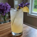 A tall glass of Honey Lavender Lemonade filled with ice, garnished with a lemon slice and fresh lavender sprigs.