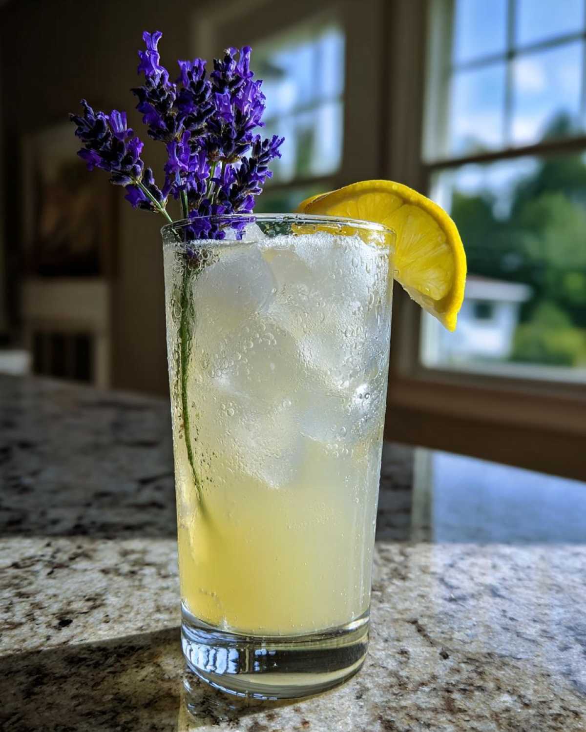 A tall glass of Honey Lavender Lemonade filled with ice, garnished with a lemon slice and fresh lavender sprigs.