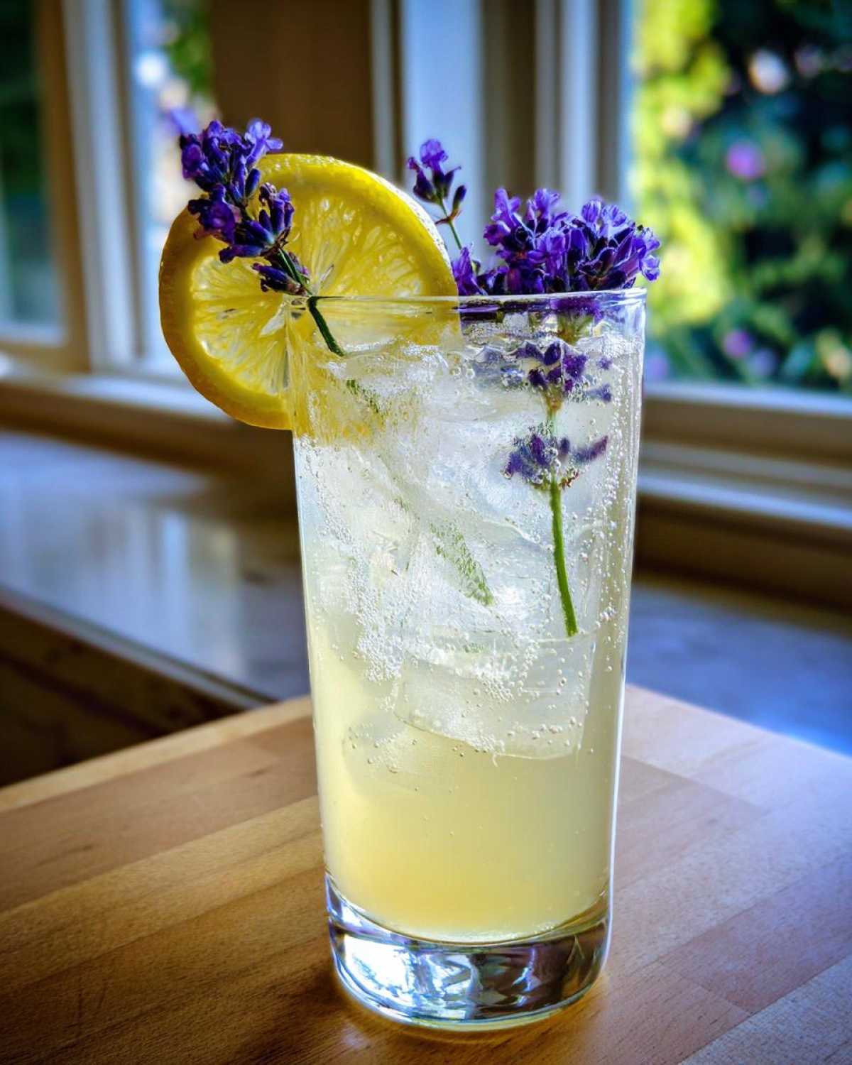 A tall glass of Honey Lavender Lemonade filled with ice, garnished with a lemon slice and fresh lavender sprigs.