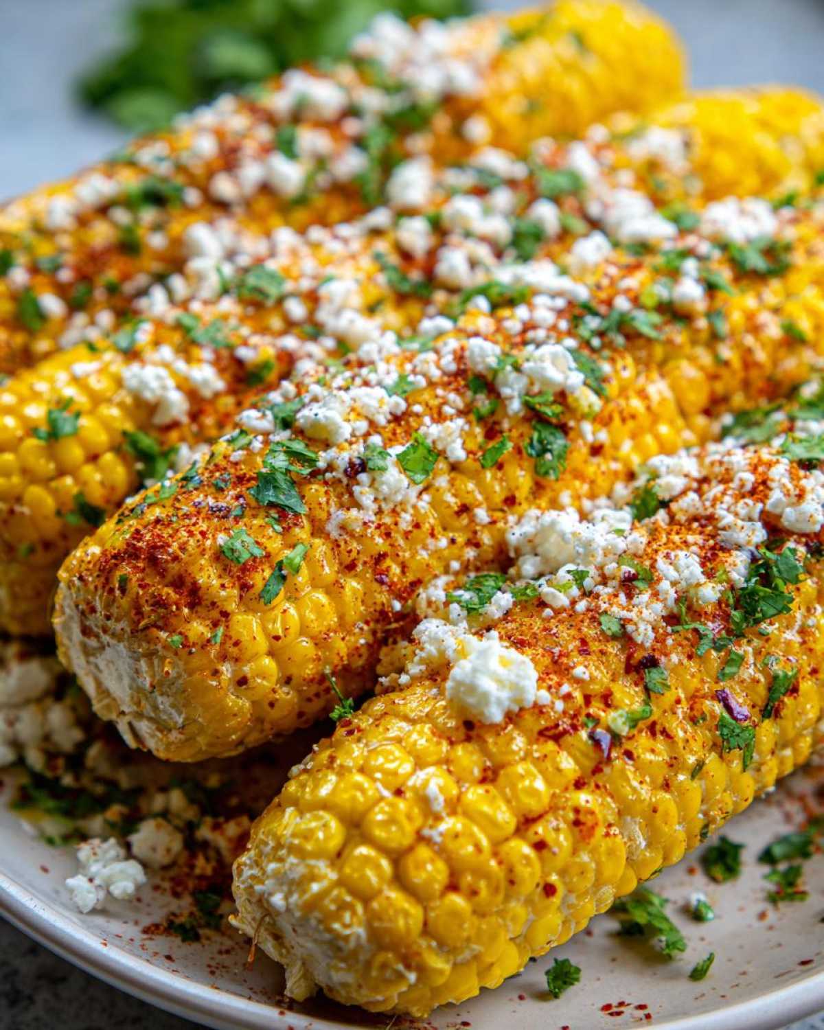 Close-up of Instant Pot Mexican street corn on a plate, topped with crumbled cheese, chili powder, and fresh cilantro.