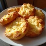 A close-up of several golden-brown Keto Cloud Bread buns piled on a white plate, showcasing their fluffy texture.