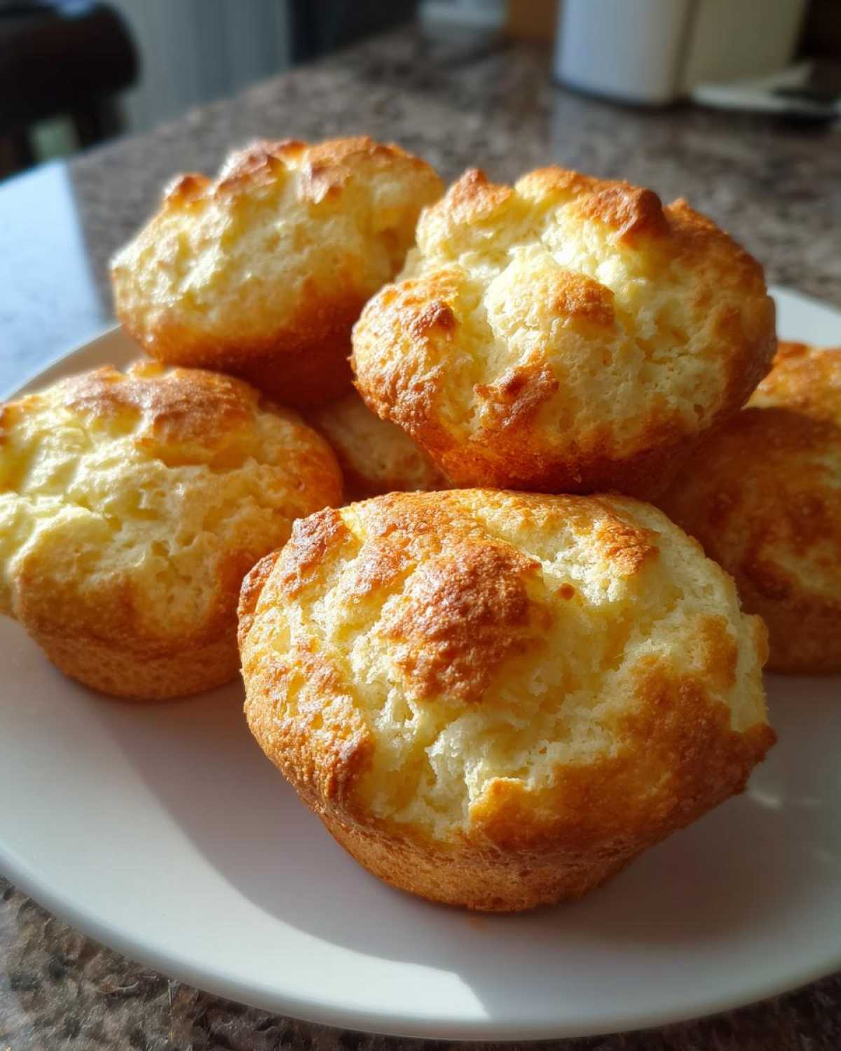 A close-up of fluffy, golden-brown Keto Cloud Bread muffins piled on a white plate.