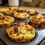 Close-up of freshly baked Keto Egg Muffins in a muffin tin, featuring bacon, red and green peppers.