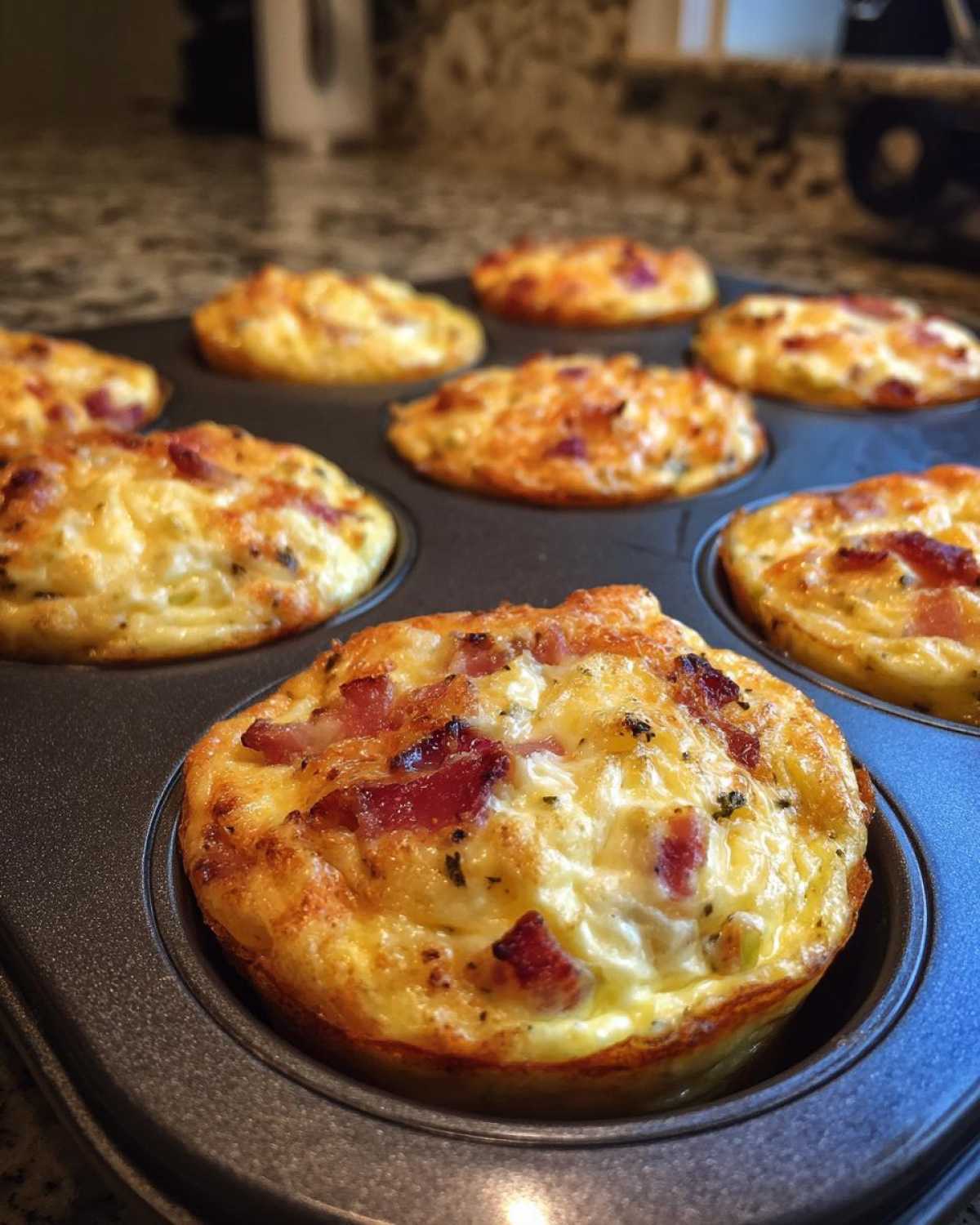 A close-up of freshly baked Keto Egg Muffins with bacon pieces in a muffin tin.