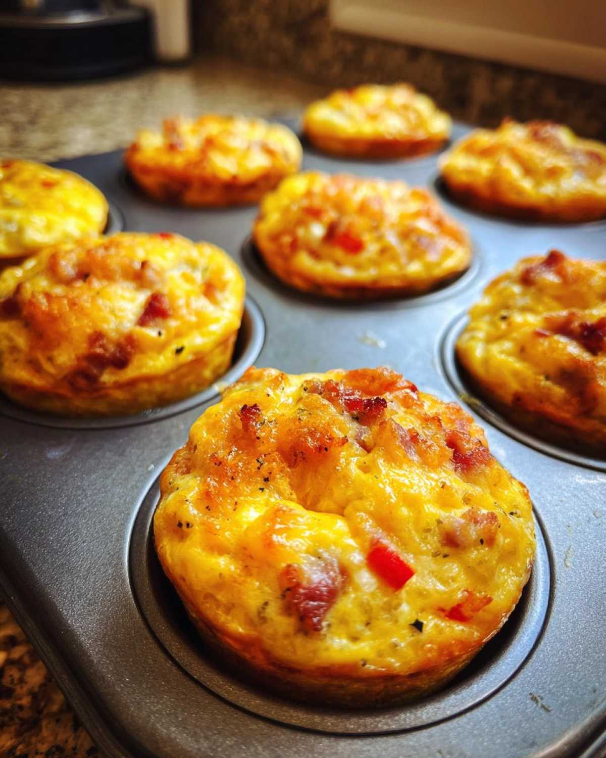 Close-up of freshly baked Keto Egg Muffins with bacon and red peppers in a muffin tin.
