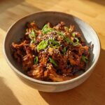 A close-up of a bowl filled with savory Korean BBQ Jackfruit (Vegan), garnished with sesame seeds and green onions.