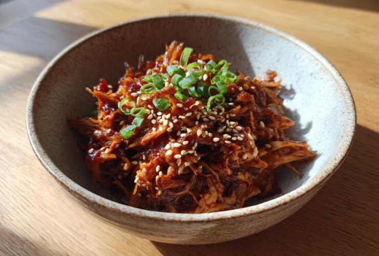 A close-up of delicious vegan Korean BBQ Jackfruit, garnished with sesame seeds and green onions in a rustic bowl.