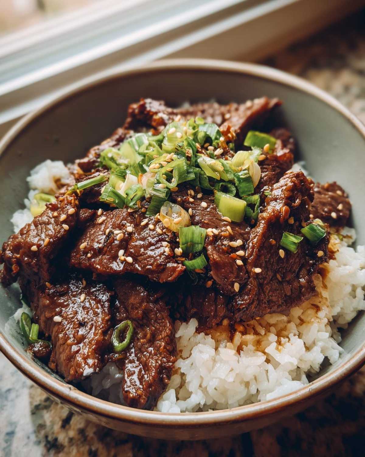 A close-up of a Korean Beef Bowl (Bulgogi) with tender marinated beef slices served over white rice and topped with chopped green onions and sesame seeds.
