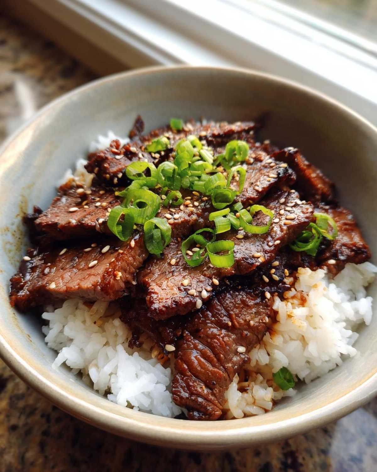 A close-up of a Korean Beef Bowl (Bulgogi) featuring tender marinated beef slices over fluffy white rice, topped with chopped green onions and sesame seeds.
