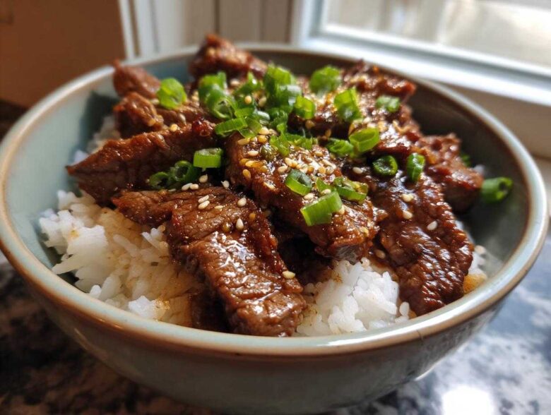 A close-up of a Korean Beef Bowl (Bulgogi) with tender marinated beef slices over white rice, topped with sesame seeds and chopped green onions.